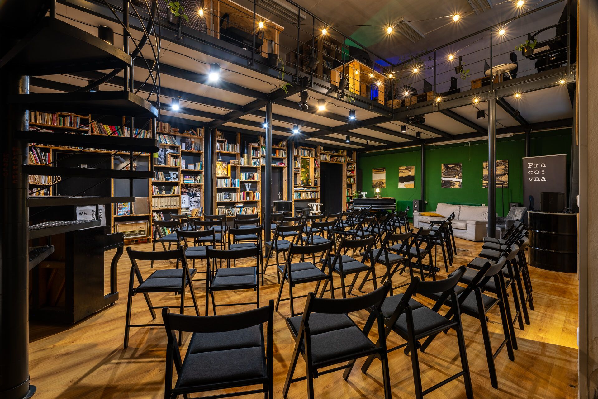 Loft s židlemi pro publikum a knihovnou v pozadí